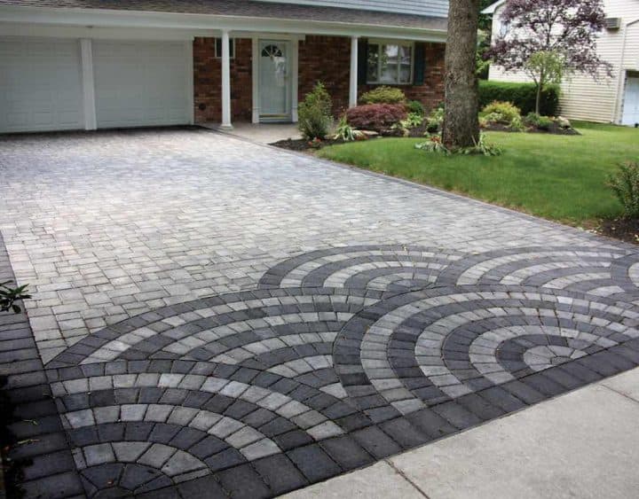 Driveway with a circular pattern of gray and black pavers in front of a brick house and garage.