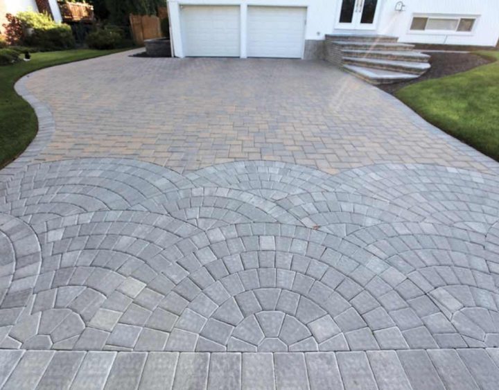 A paved driveway with intricate gray stone patterns leads to a white garage with two doors.