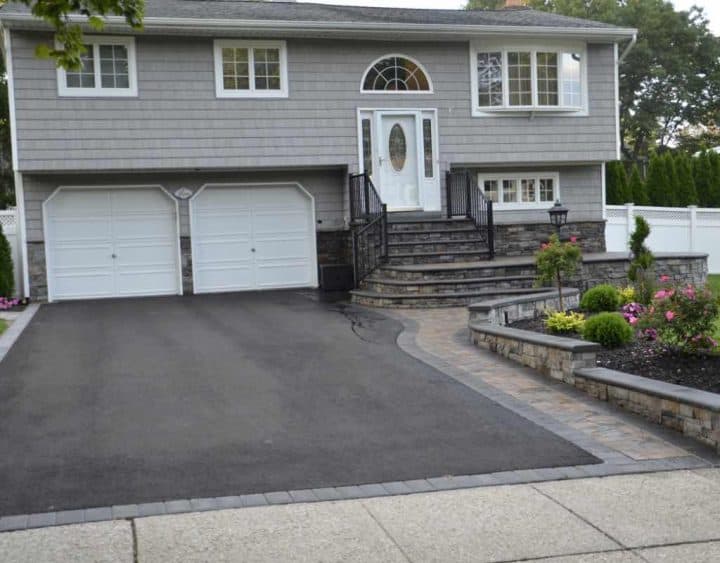 A gray split-level house with a two-car garage, stairs leading to the front door, and a landscaped front yard with a paved driveway and walkway.