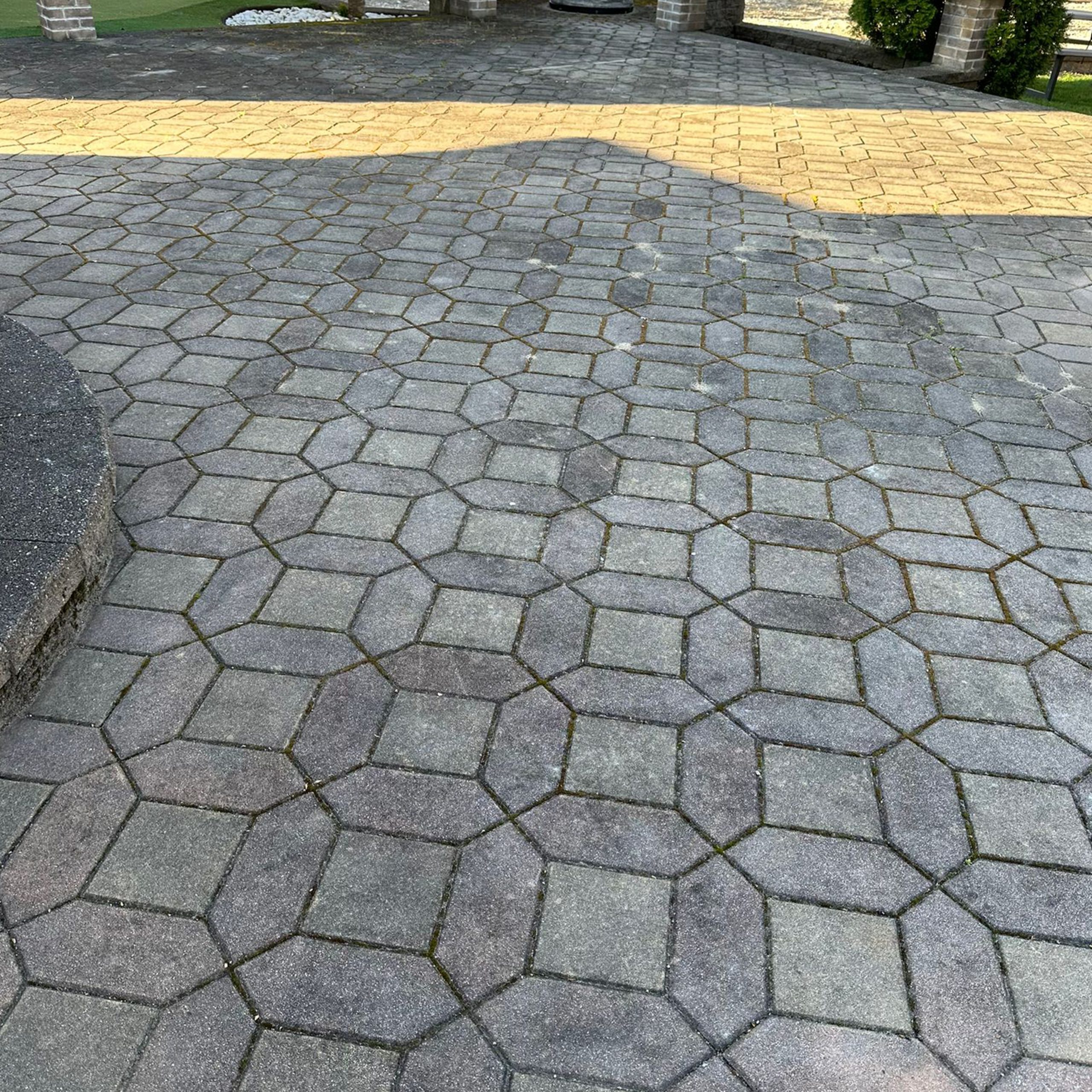 Paved walkway with interlocking geometric stone tiles, some with moss in the joints, leading toward an area with a different colored paving pattern in the background.